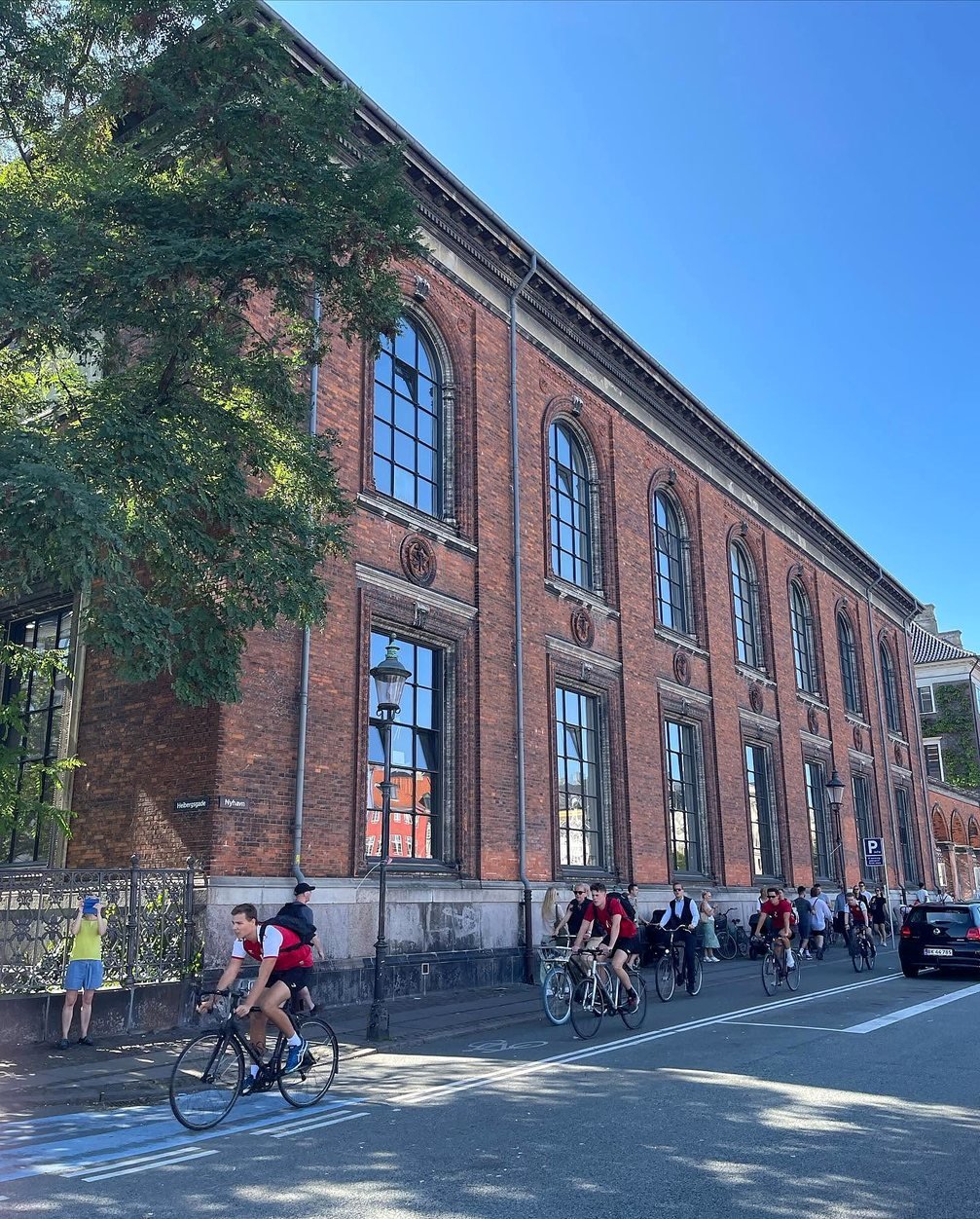 Ciclistas passando por prédio histórico de tijolos perto de Nyhavn