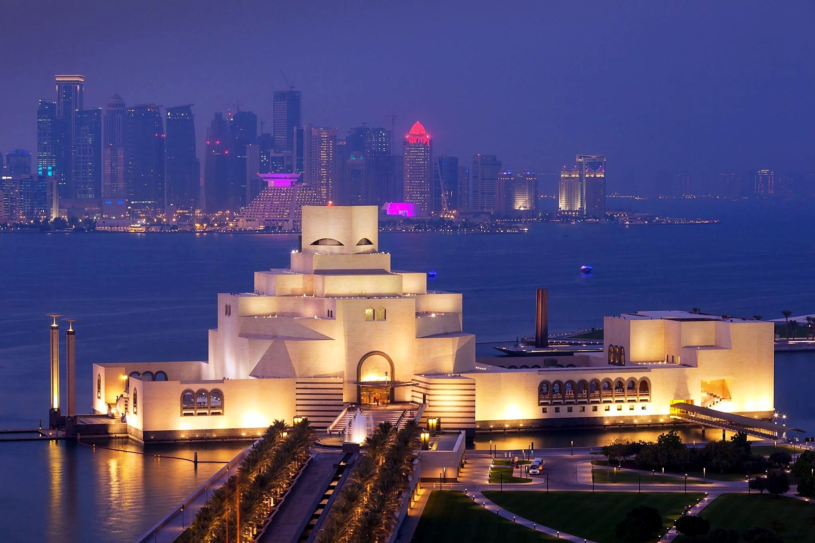 Museu de Arte Islâmica iluminado à noite, com o skyline de Doha ao fundo