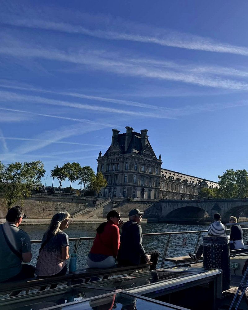 Turistas em barco no Sena com o Louvre ao fundo