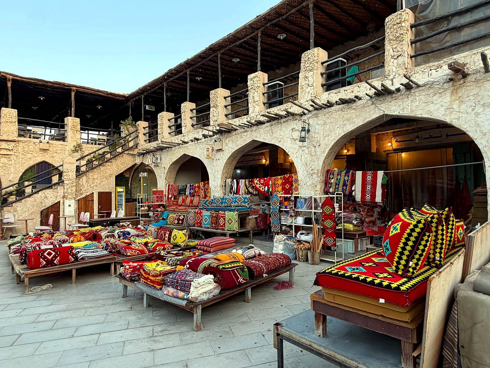 Lojas de tecidos e almofadas coloridas sob os arcos do Souq Waqif