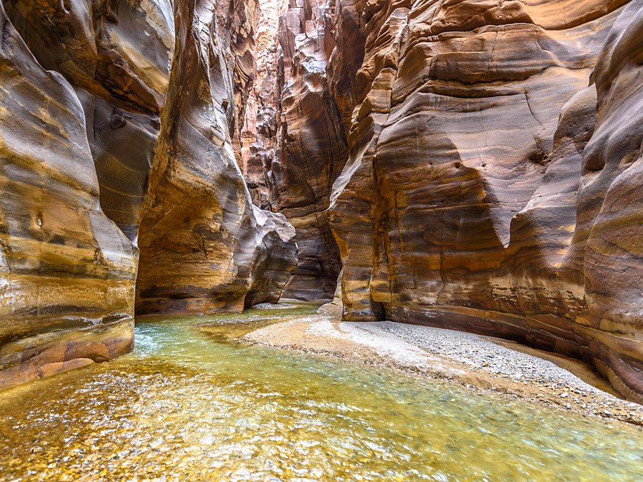 Rio correndo entre os paredões de pedra do cânion Wadi Mujib, na Jordânia