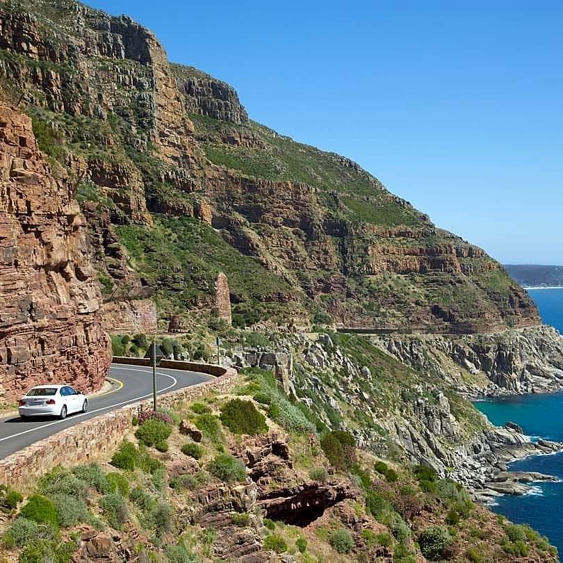 Carro na estrada Chapman's Peak Drive, entre o penhasco e o mar