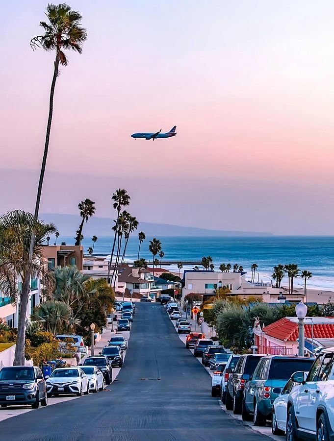 Avião chegando a Los Angeles sobre uma rua com palmeiras e o mar ao fundo