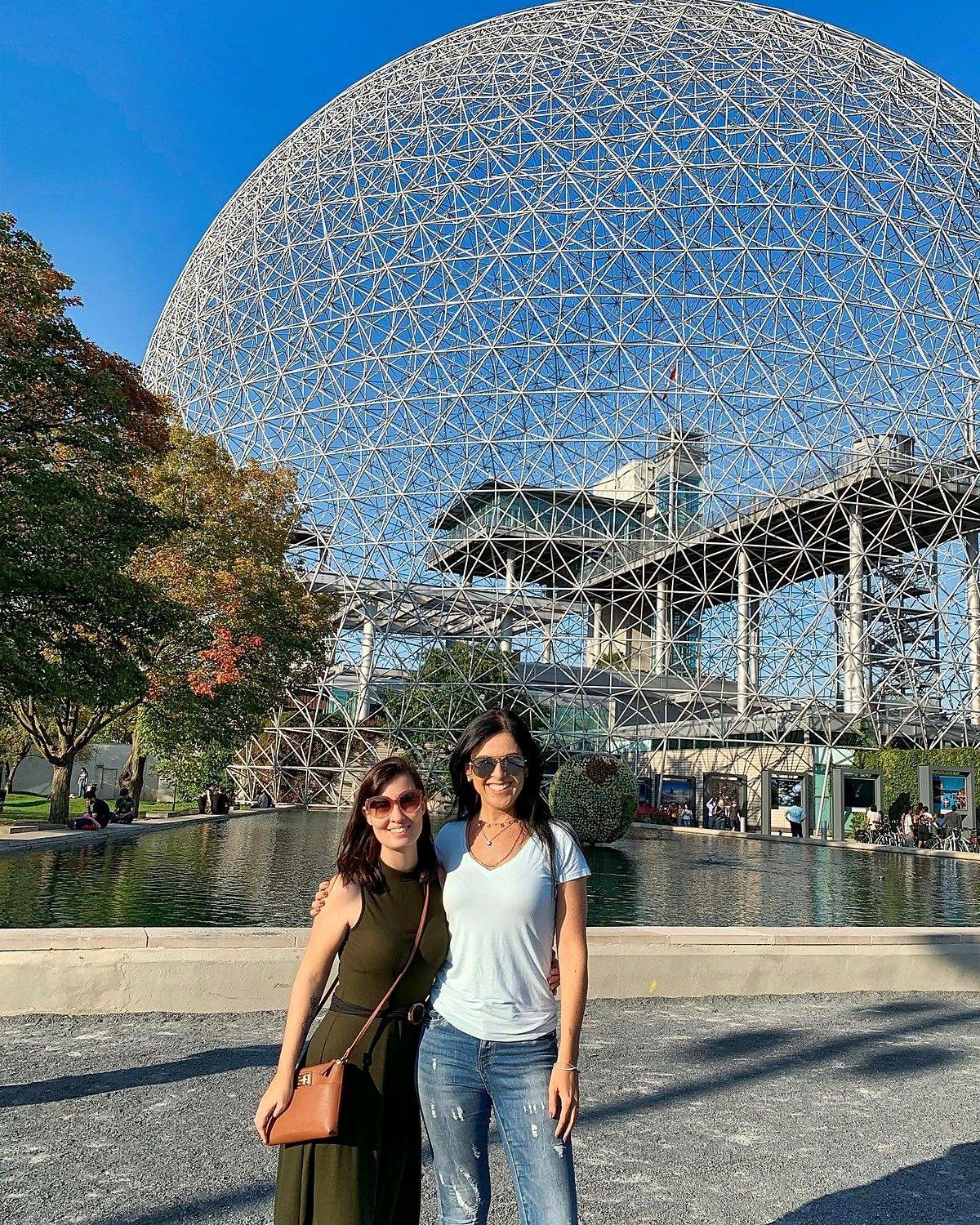Viajantes em frente à Biosfera de Montreal com árvores começando a mudar de cor