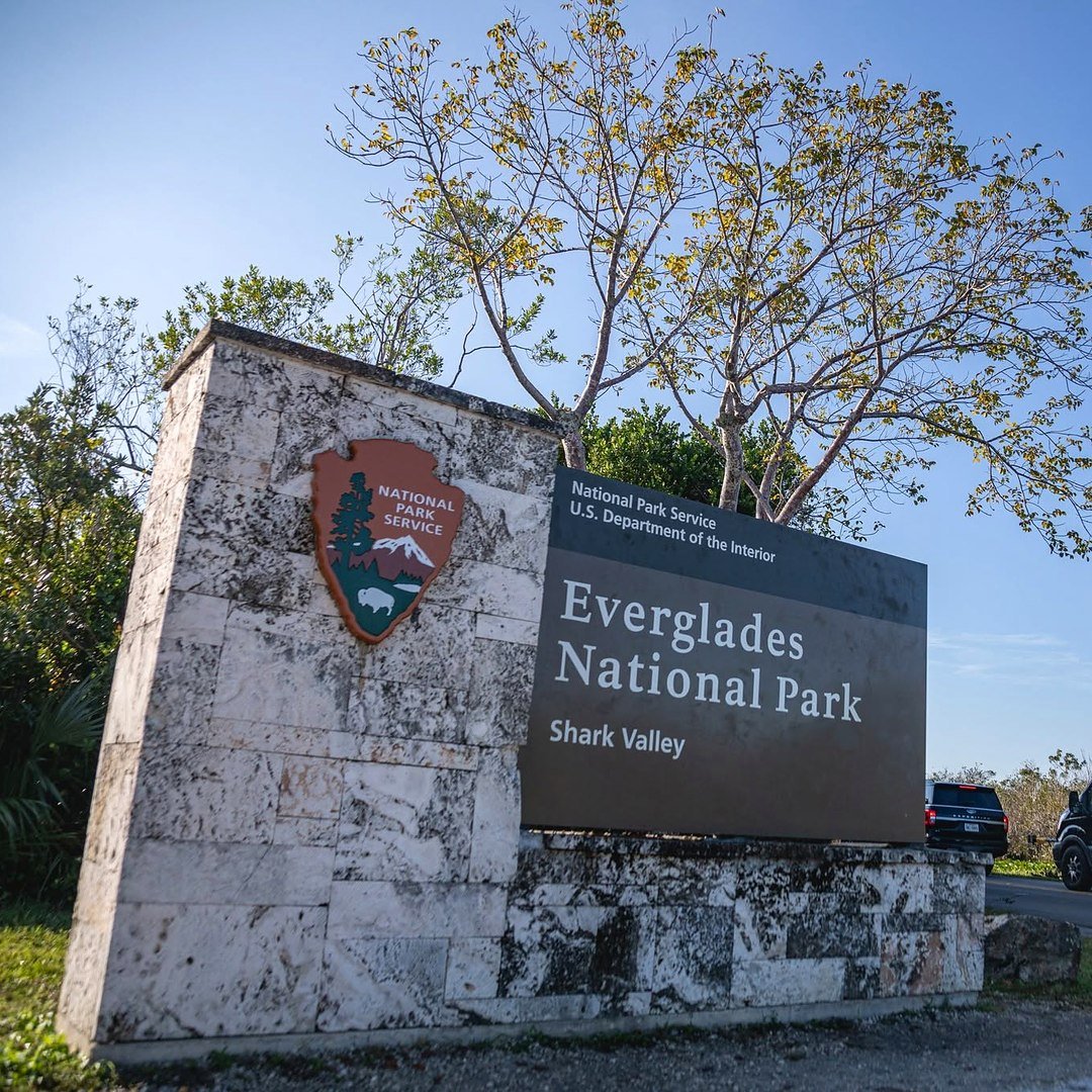 Placa de entrada de Shark Valley, no Parque Nacional do Everglades, com van estacionada ao lado