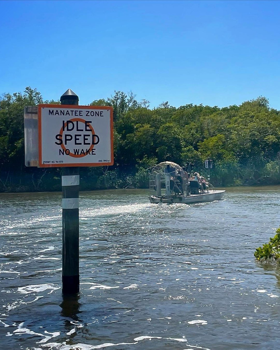 Placa de zona de peixe-boi em um canal de mangue, com aerobarco levando turistas ao fundo