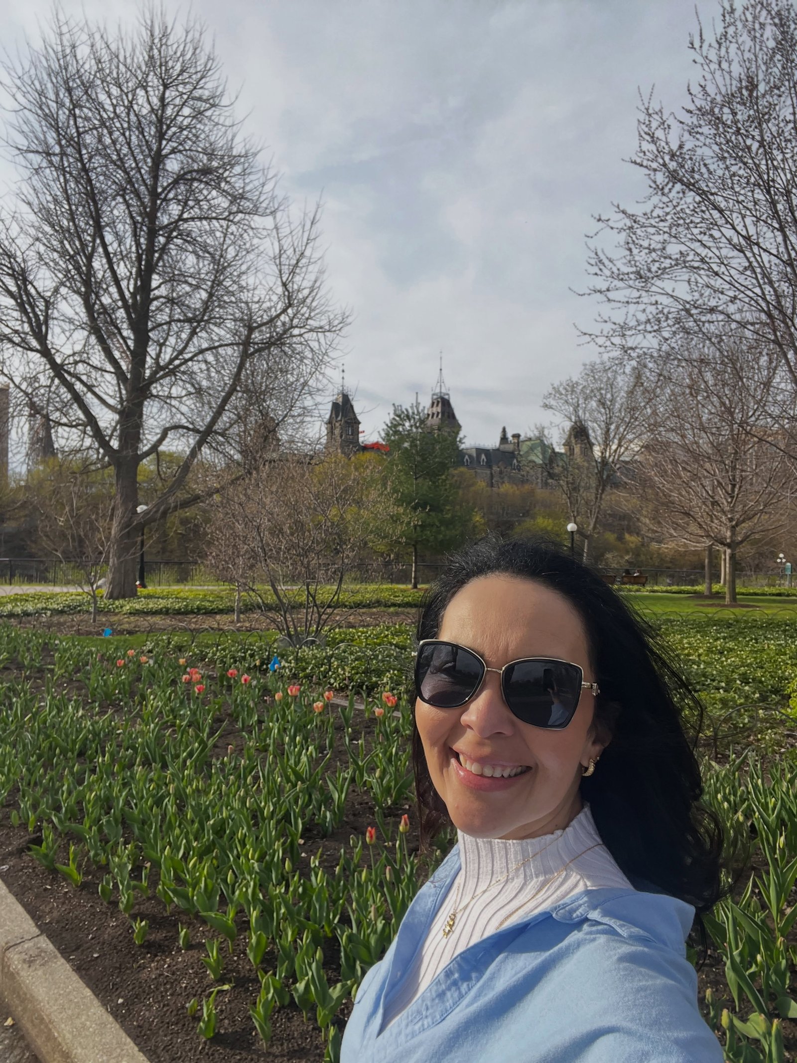 Diana Carvalho, guia brasileira em Ottawa, entre tulipas com os prédios do Parlamento ao fundo