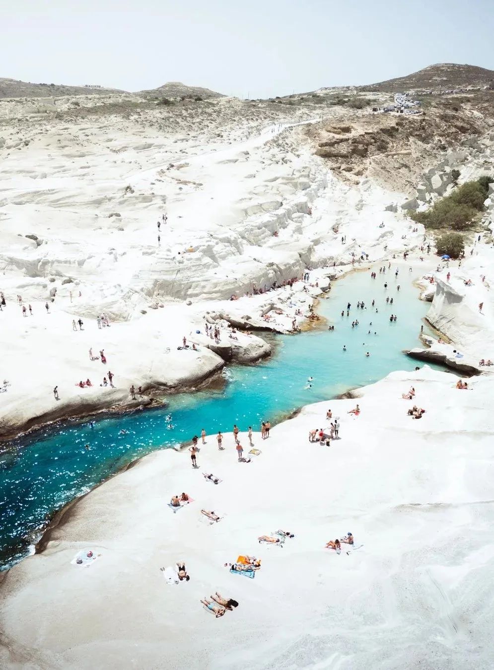 Rochas brancas vulcânicas da praia de Sarakiniko, em Milos, com banhistas e mar azul-turquesa