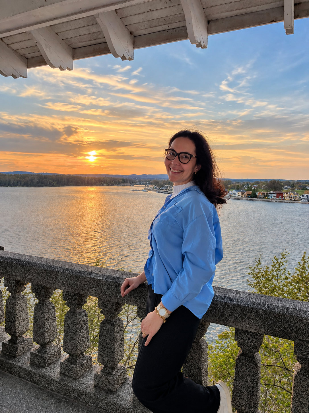 Diana Carvalho sorrindo em um mirante à beira do rio ao pôr do sol