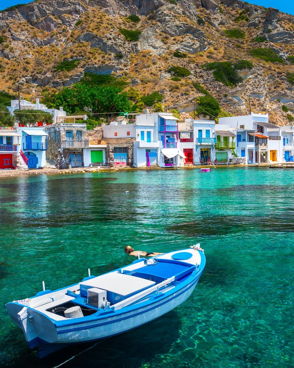 Casinhas coloridas de pescadores e barco de madeira na água transparente em Klima, Milos