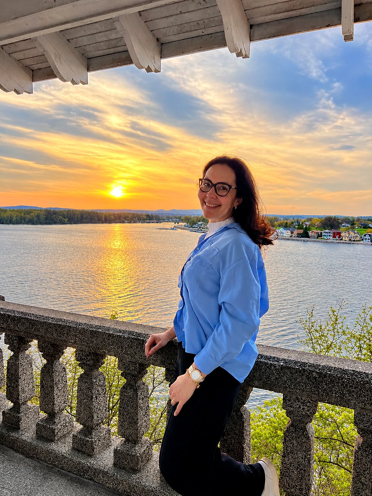 Diana Carvalho sorrindo em um mirante à beira do lago ao pôr do sol