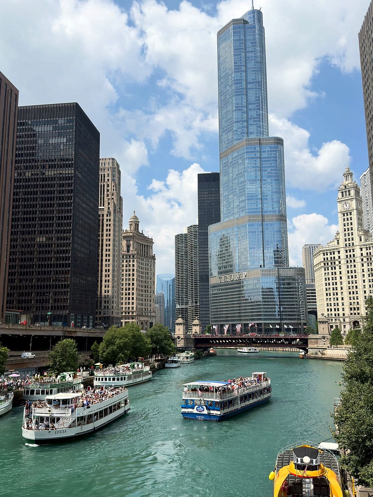 Barcos de passeio no rio Chicago entre arranha-céus, com a torre do relógio do Wrigley Building