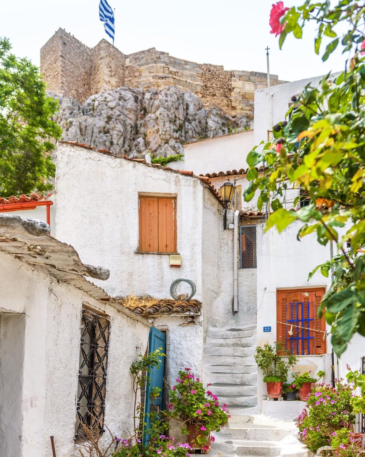 Ruela de casas brancas com flores em Plaka, com a rocha da Acrópole ao fundo