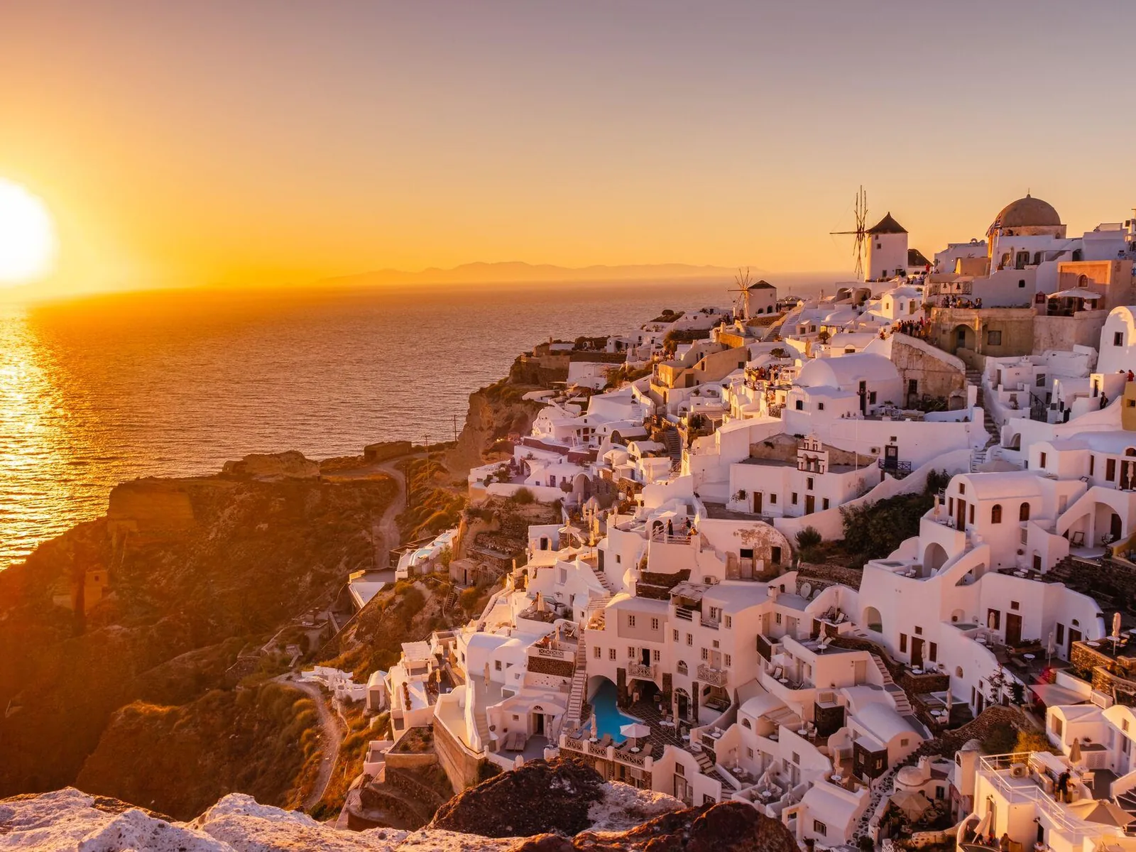 Pôr do sol em Oia, Santorini, com os moinhos de vento e as casas brancas iluminadas pelo sol