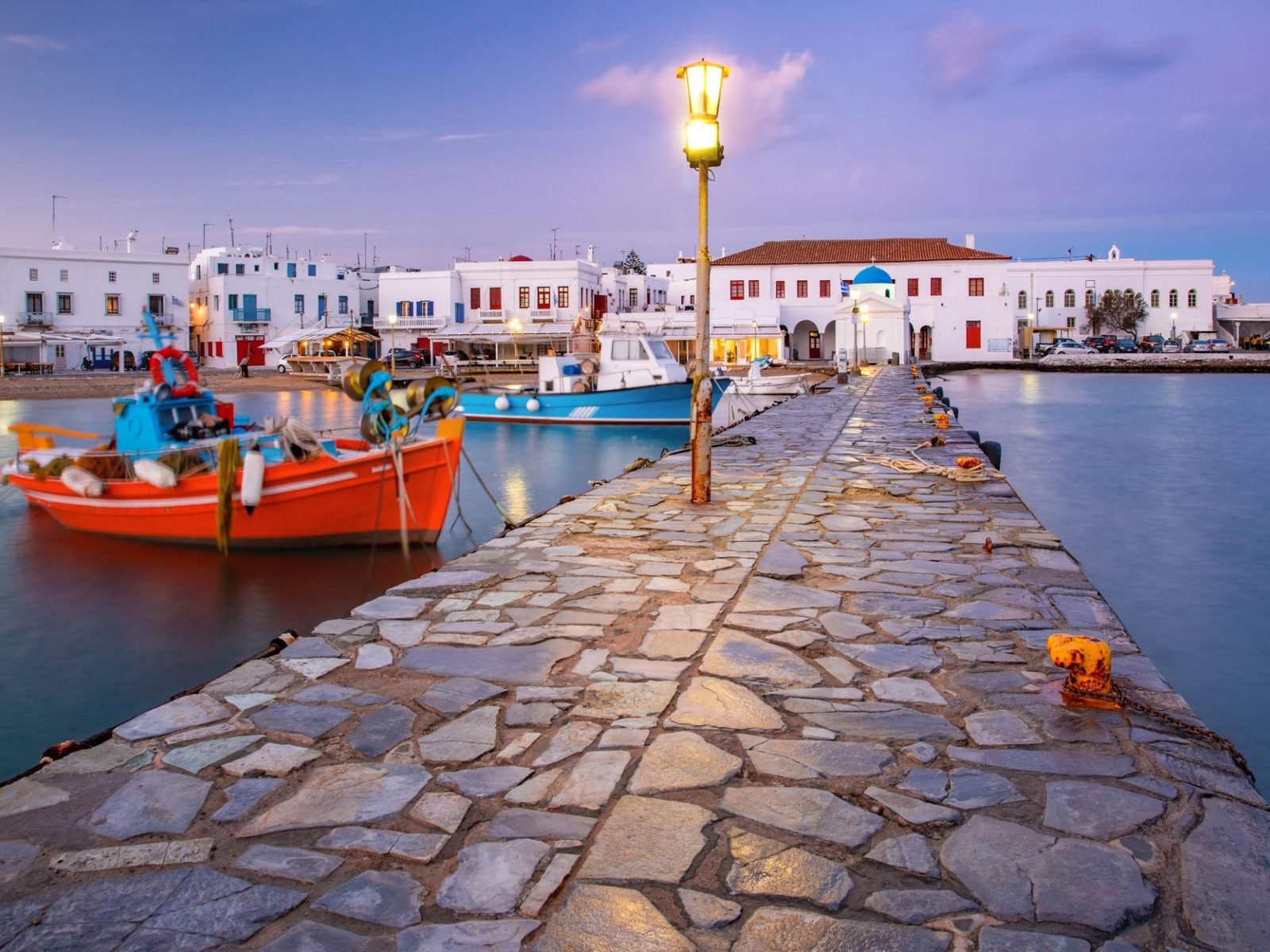 Barcos de pesca coloridos no Porto Antigo de Mykonos ao entardecer, com as casas brancas de Chora ao fundo