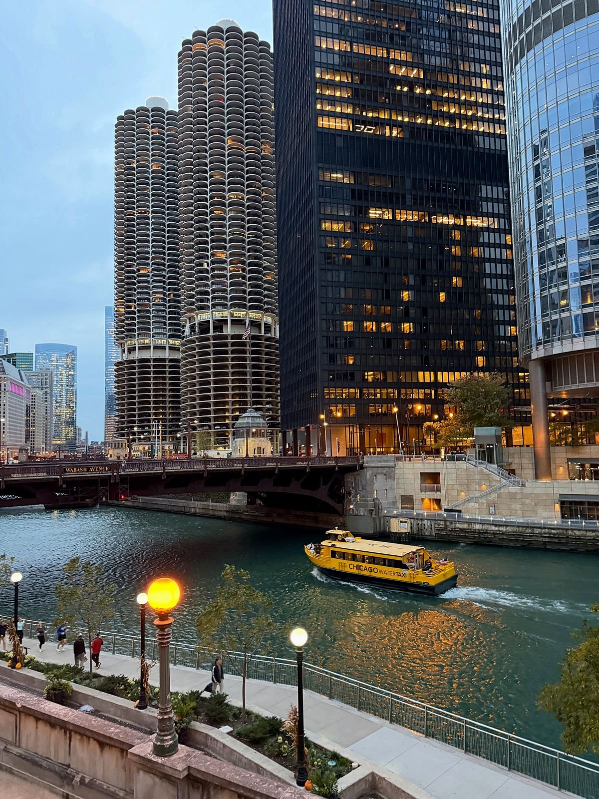 Riverwalk de Chicago ao entardecer, com as torres Marina City e um táxi aquático no rio