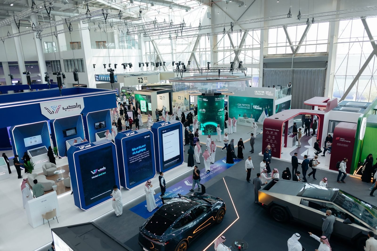 Vista do alto de um pavilhão de feira de tecnologia em Riade, com estandes e carros em exposição