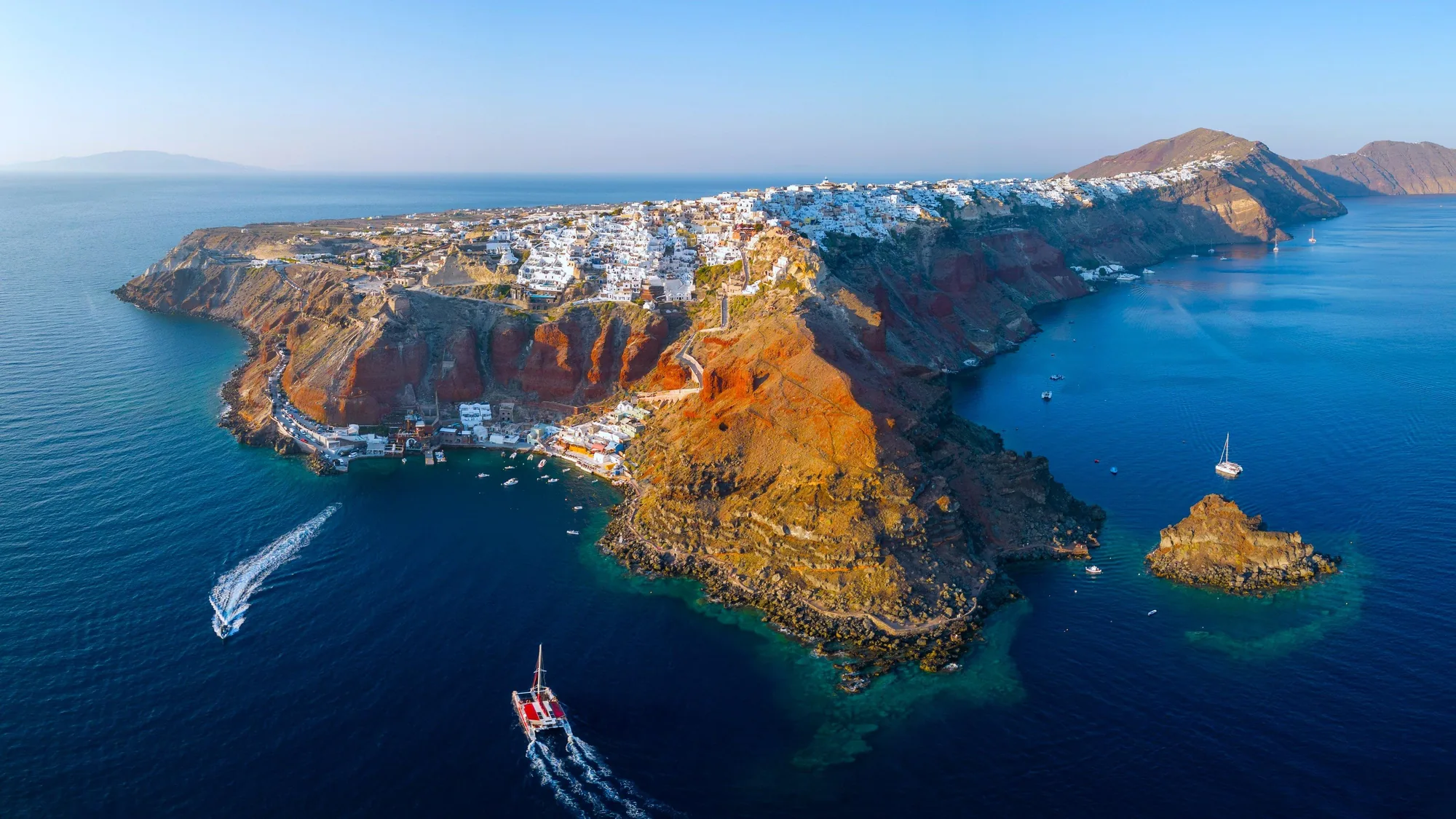 Vista aérea da caldeira de Santorini, com as vilas brancas na borda das falésias e a ilha do vulcão no centro
