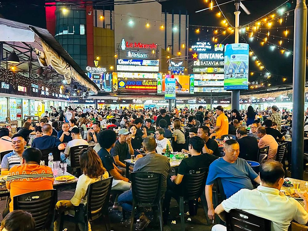 Praça de alimentação cheia à noite, com barracas iluminadas