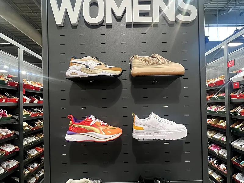 Parede de tênis femininos em loja de outlet de Orlando, com prateleiras de caixas ao fundo