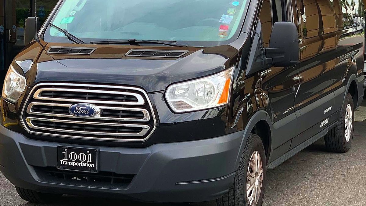 Van Ford preta com placa da 1001 Transportation estacionada em frente a um hotel