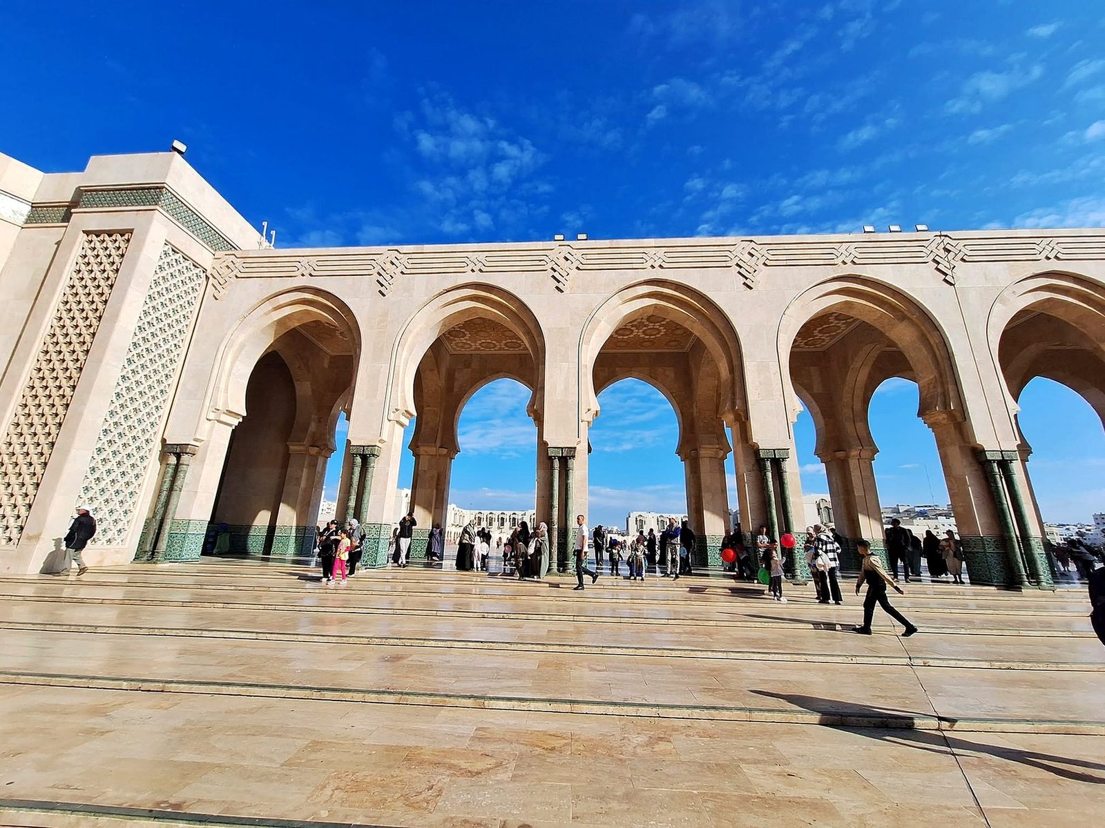 Arcadas da esplanada da Mesquita Hassan II em Casablanca, com visitantes e céu azul