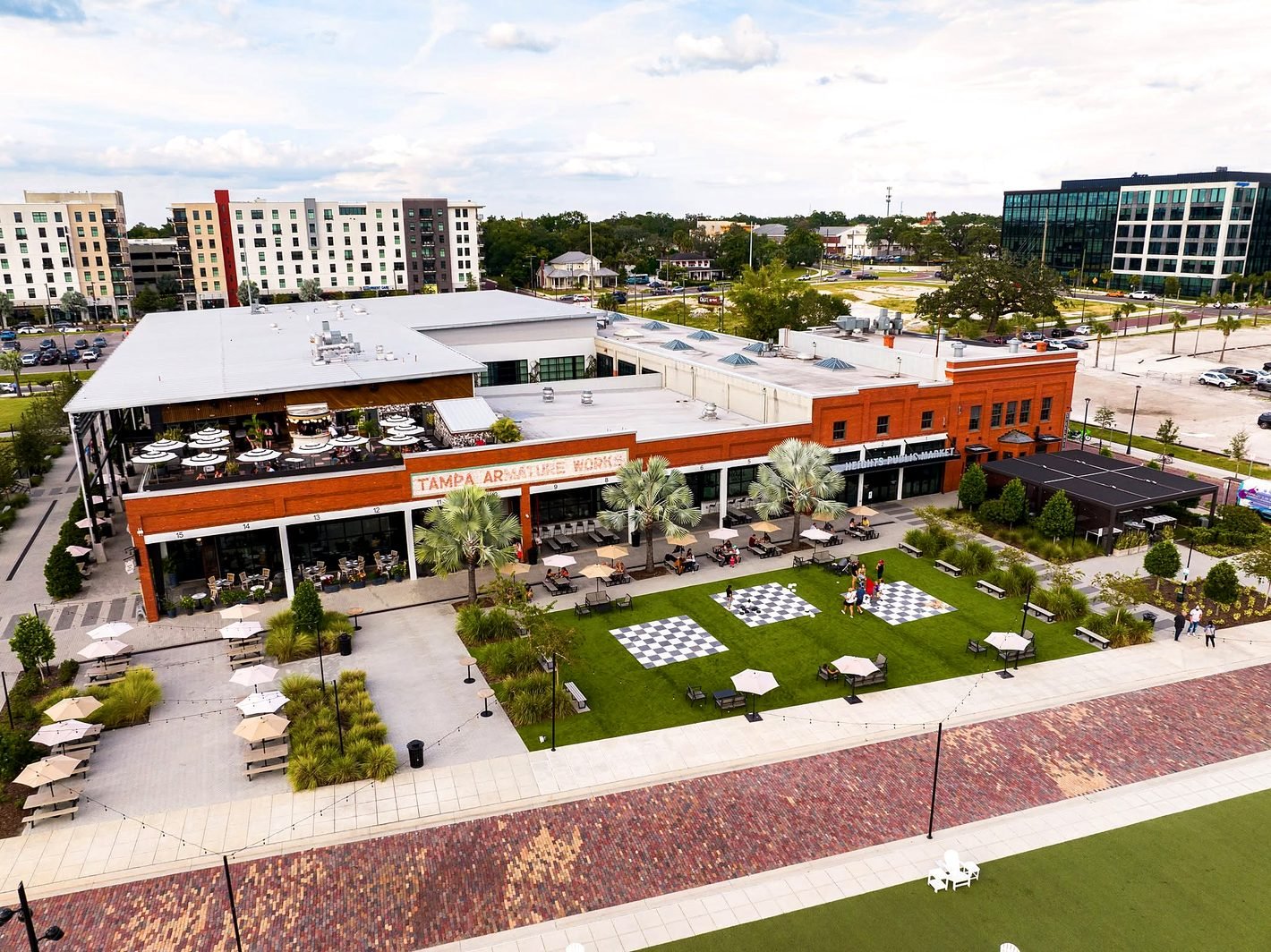 Vista aérea do Armature Works, prédio histórico de tijolos com mercado gastronômico e gramado em Tampa Heights