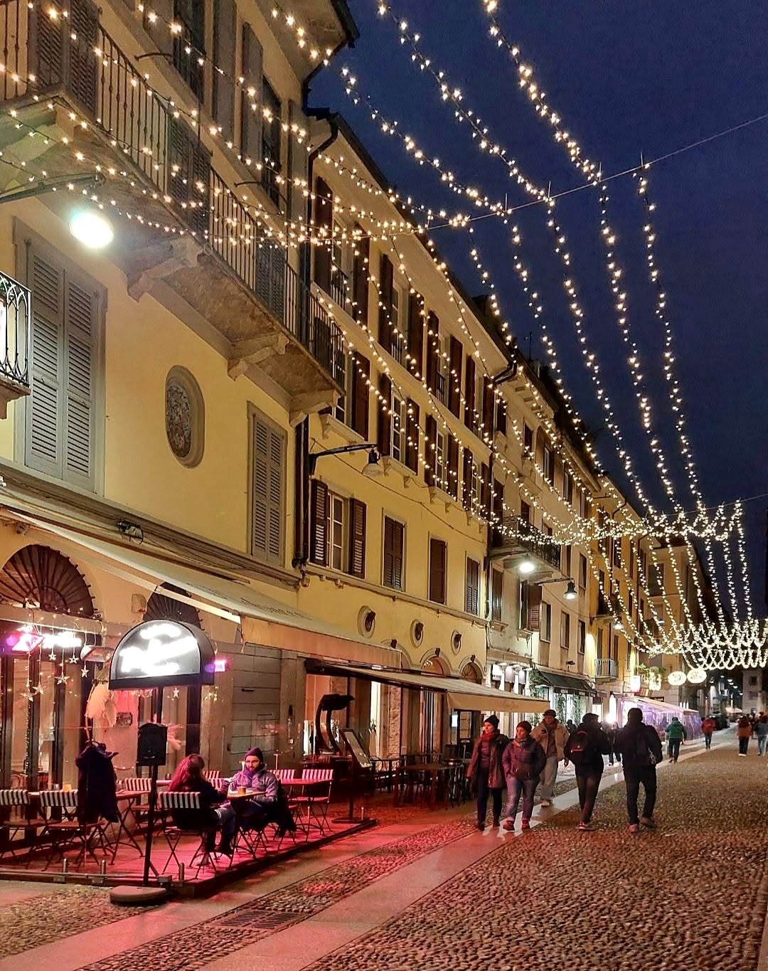 Rua de Brera em Milão à noite com luzes penduradas e mesas de bares na calçada
