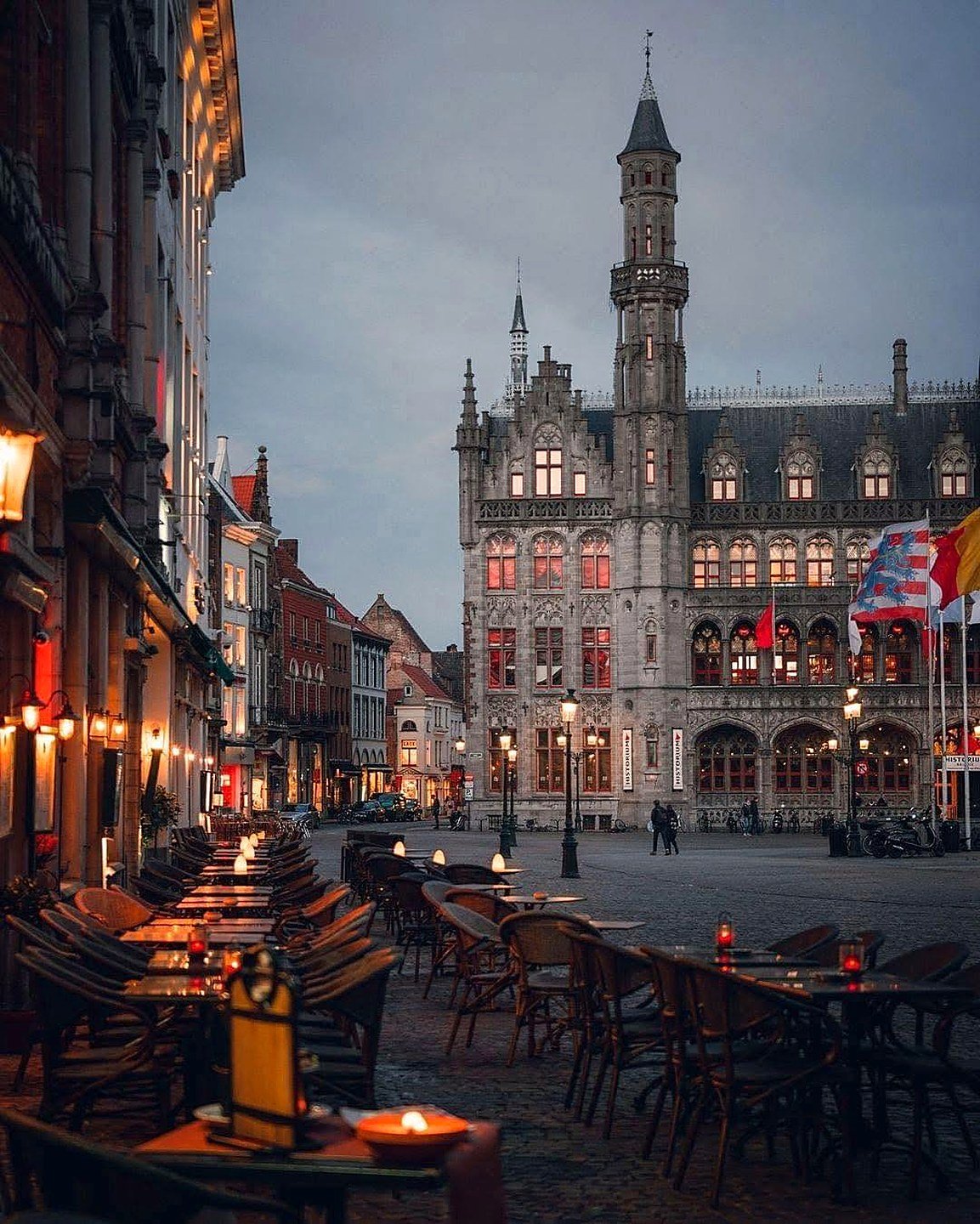 Markt de Bruges ao entardecer, com o Palácio Provincial iluminado e mesas de café na praça