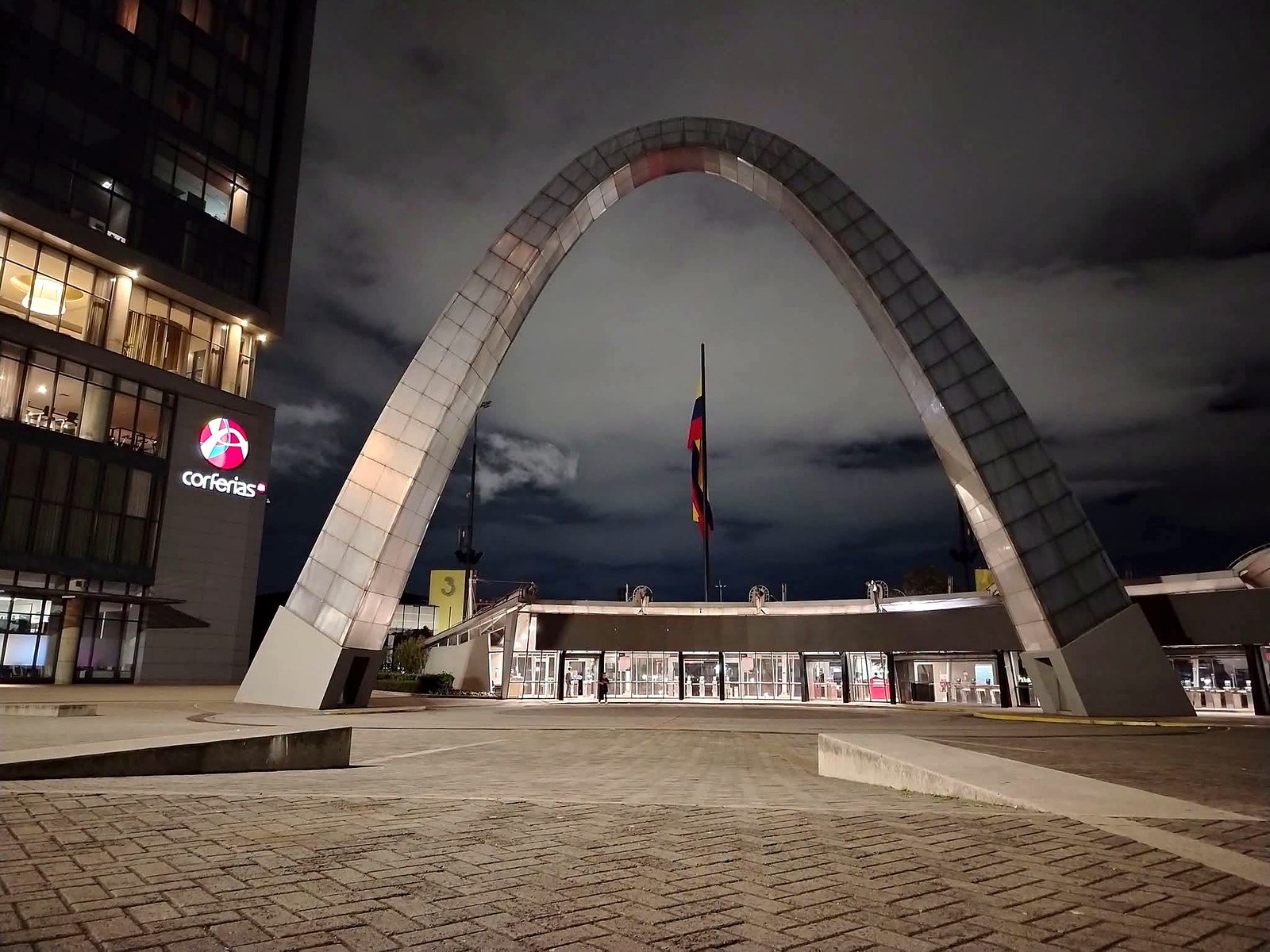 Arco da entrada principal do Corferias à noite com a bandeira da Colômbia