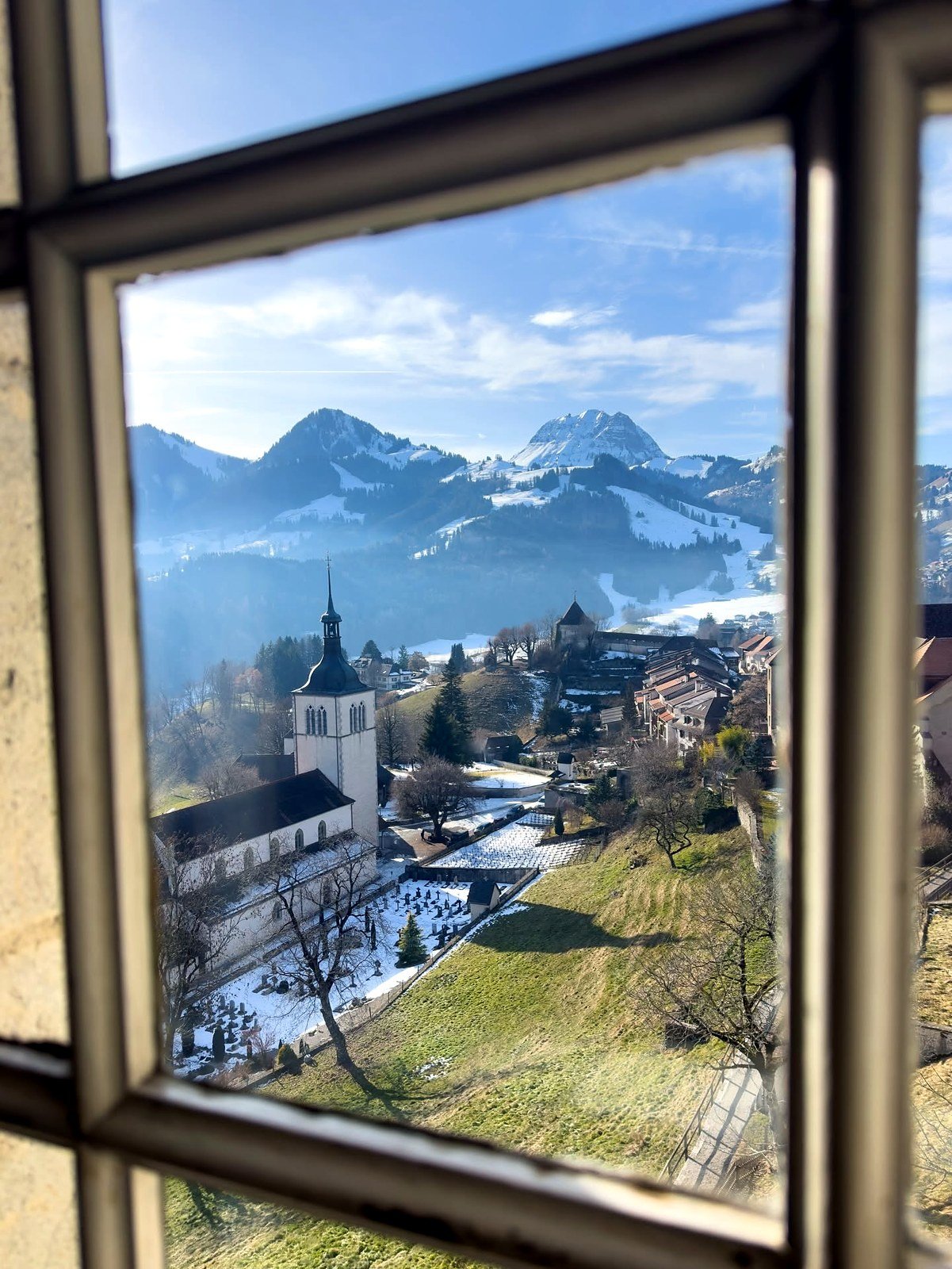 Vista da igreja e das montanhas nevadas pela janela do Castelo de Gruyères