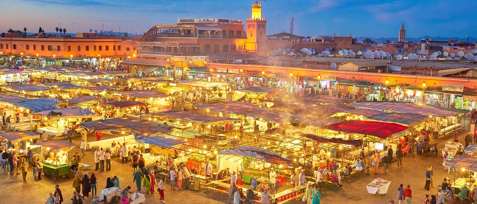 Praça Jemaa el-Fnaa ao entardecer, com as barracas de comida acesas e o minarete ao fundo, em Marrakech