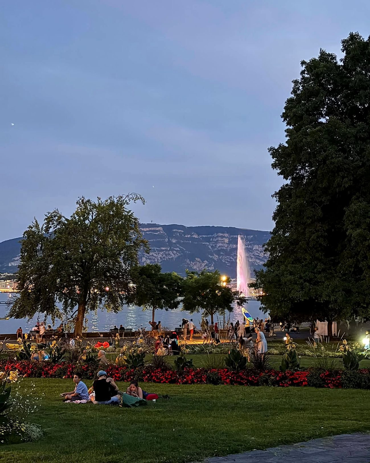 Jet d'Eau iluminado ao entardecer visto de um parque à beira do Lago Léman, em Genebra