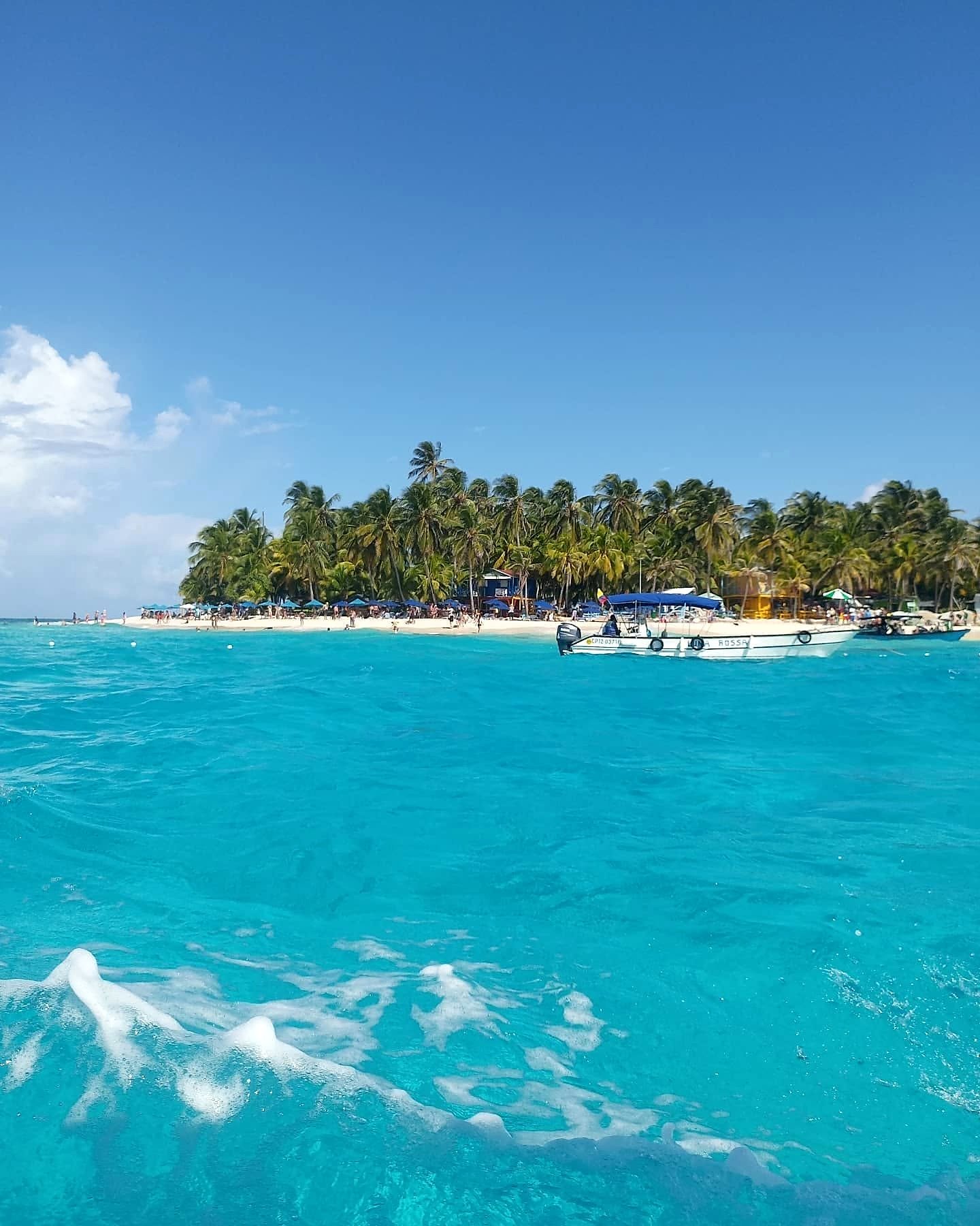 Johnny Cay, ilhota de coqueiros e areia branca com barco no mar azul de San Andrés