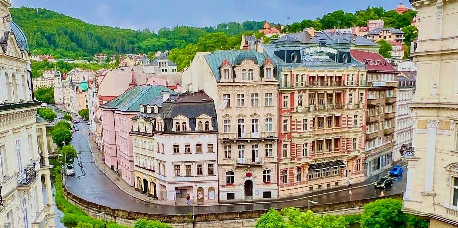 Curva do rio Teplá com prédios históricos coloridos e colinas verdes em Karlovy Vary