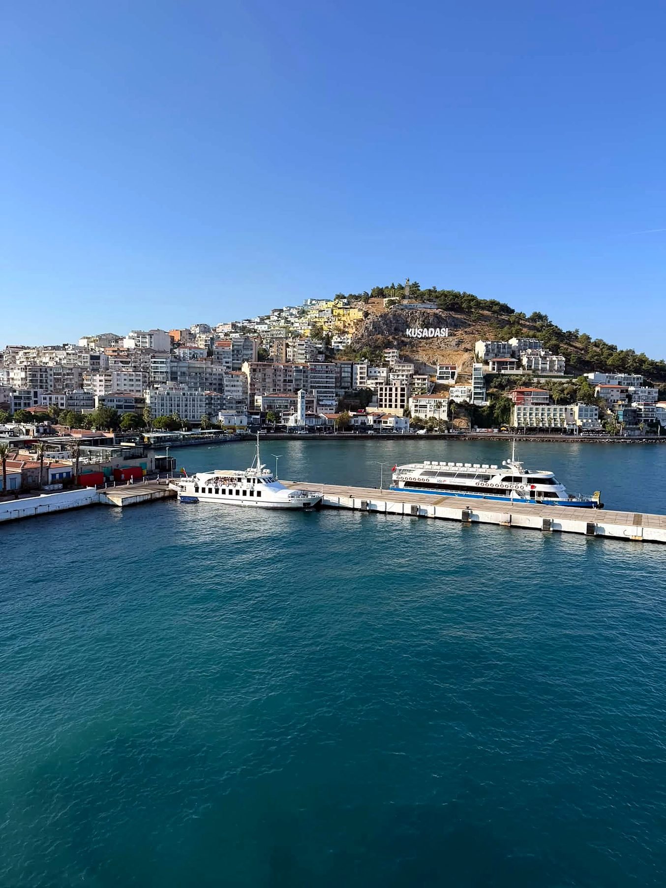 Porto de Kuşadası com barcos atracados e a cidade na encosta, no litoral do Egeu