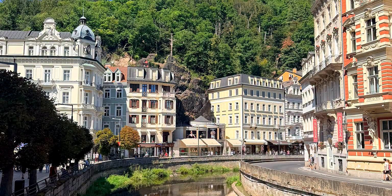 Rio Teplá refletindo os prédios históricos do centro de Karlovy Vary, ao pé da colina arborizada