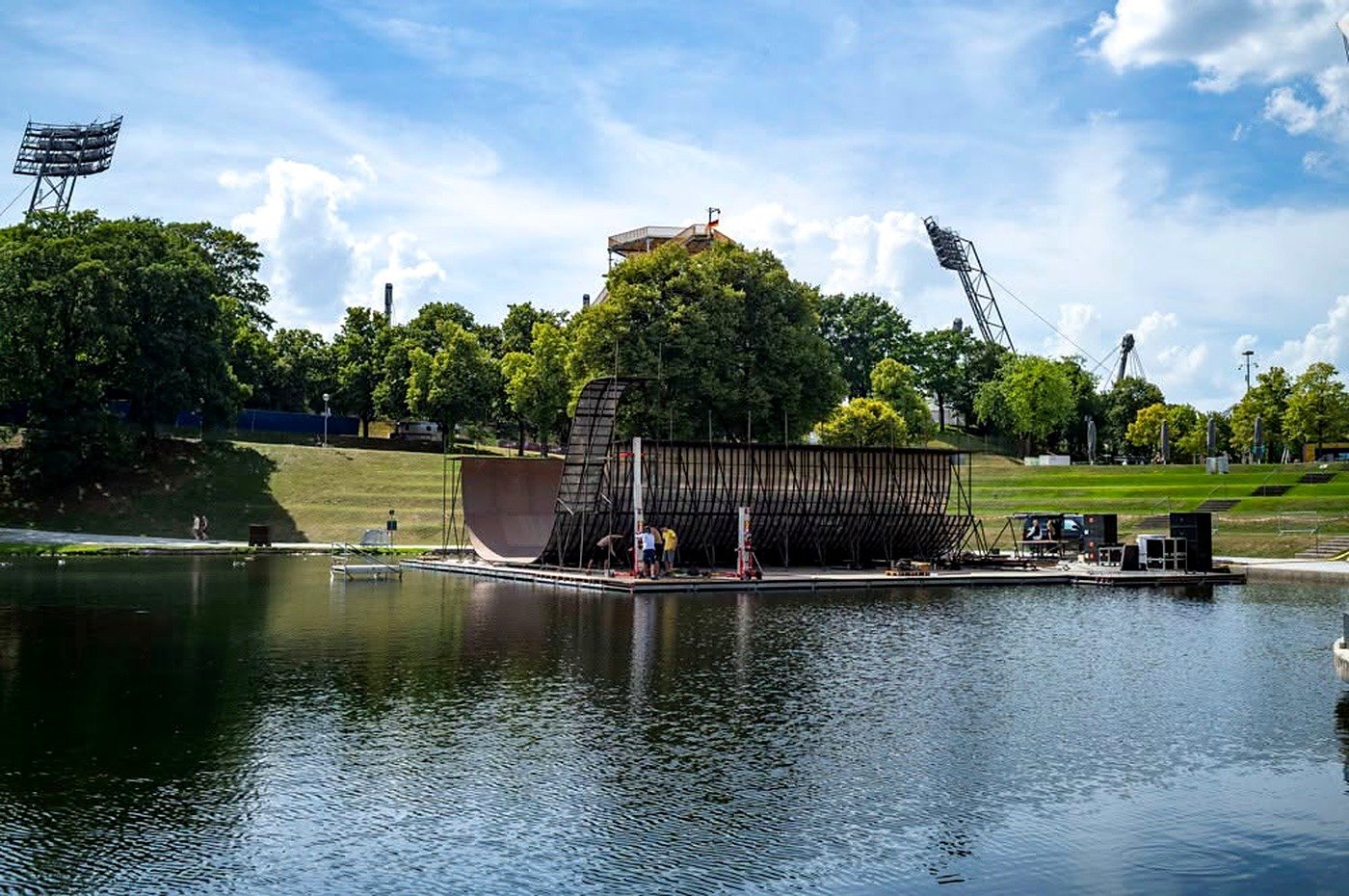 Lago do Olympiapark de Munique com estrutura de eventos e estádio ao fundo