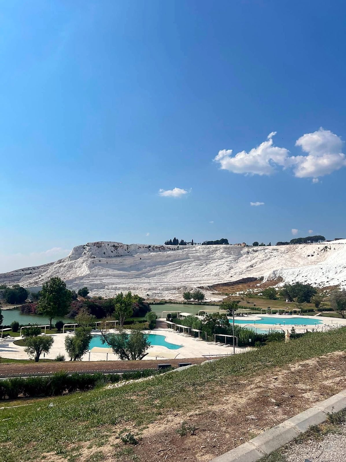 Encosta branca de travertino de Pamukkale vista do vilarejo, com lago e piscinas