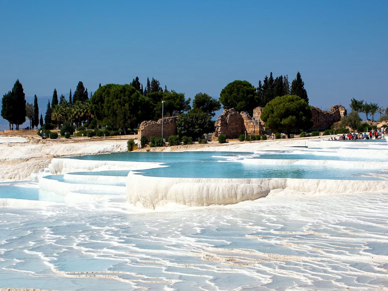 Piscinas de travertino brancas com água azul em Pamukkale e as ruínas de Hierápolis ao fundo