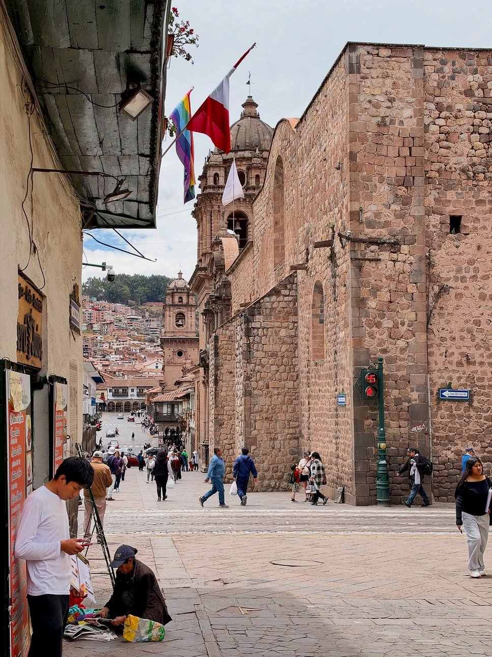 Rua do centro de Cusco com muralha de pedra e torres de igreja ao fundo