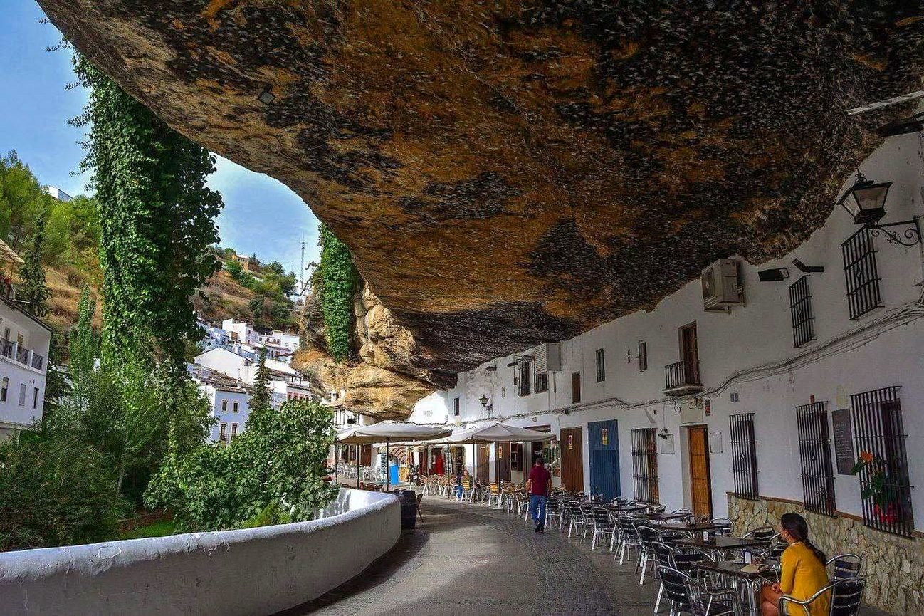 Rua de Setenil de las Bodegas com casas brancas e mesas de bar sob uma enorme rocha
