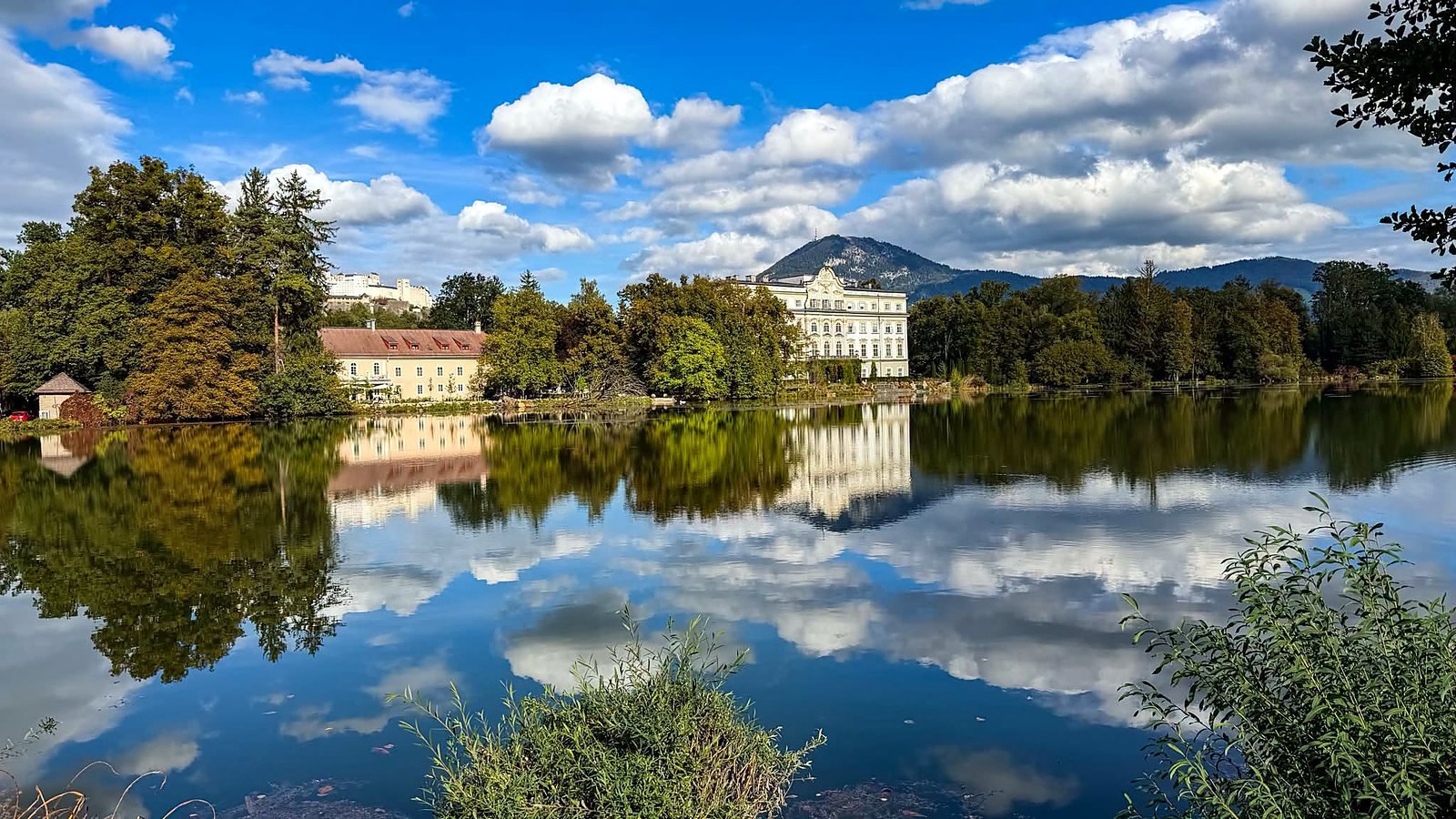 Palácio de Leopoldskron refletido no lago, com a Fortaleza de Hohensalzburg ao fundo, em Salzburgo
