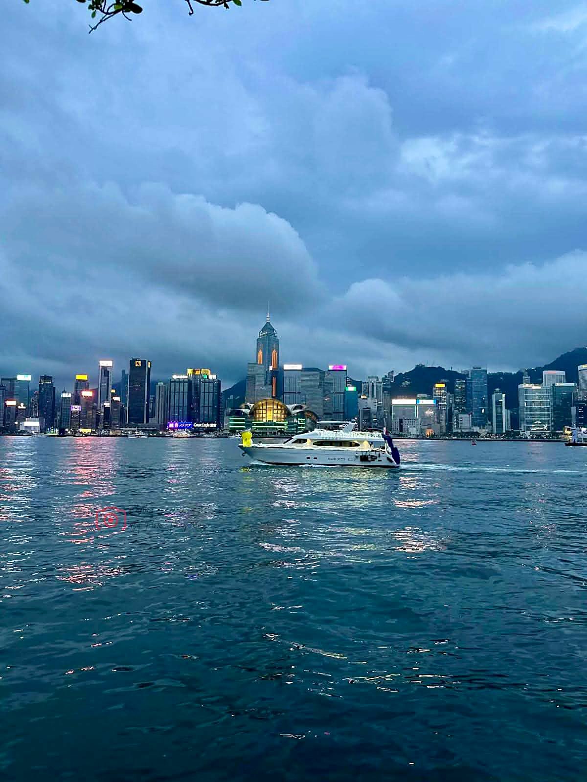 Barco cruzando o Victoria Harbour ao entardecer com o skyline iluminado