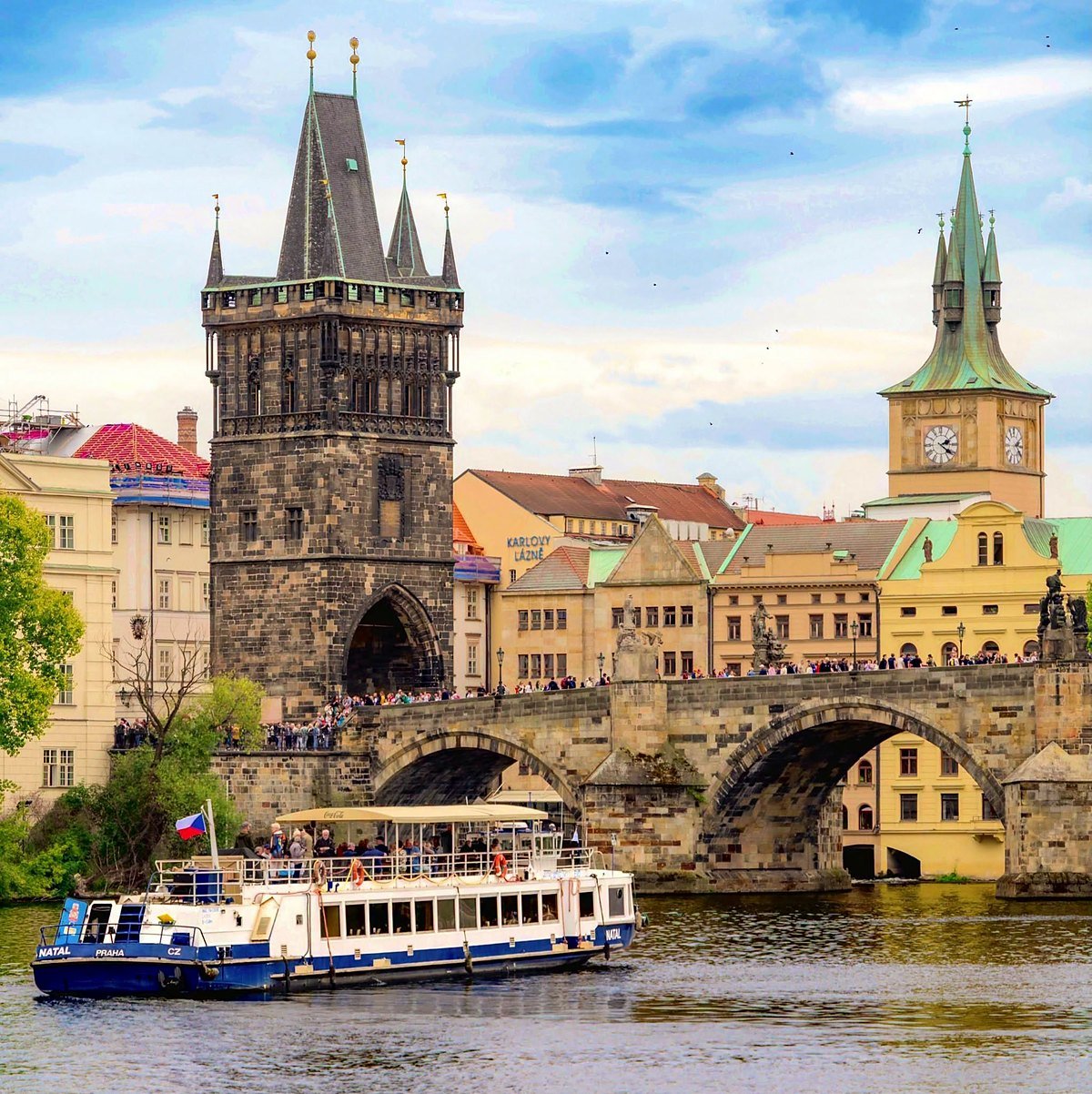 Barco de passeio no rio Vltava diante da Torre da Ponte da Cidade Velha e da Ponte Carlos