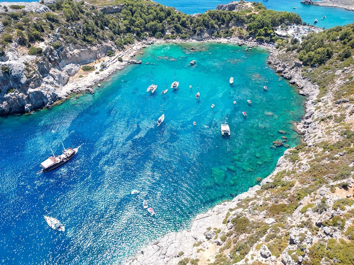 Barcos e veleiros ancorados na água cristalina de Anthony Quinn Bay, em Rodes