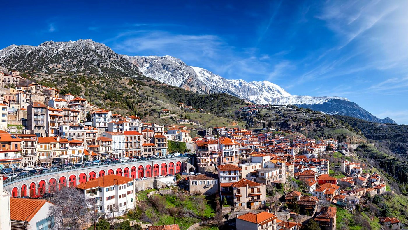 Vila de Arachova com casas de telhados vermelhos e o Monte Parnaso coberto de neve ao fundo