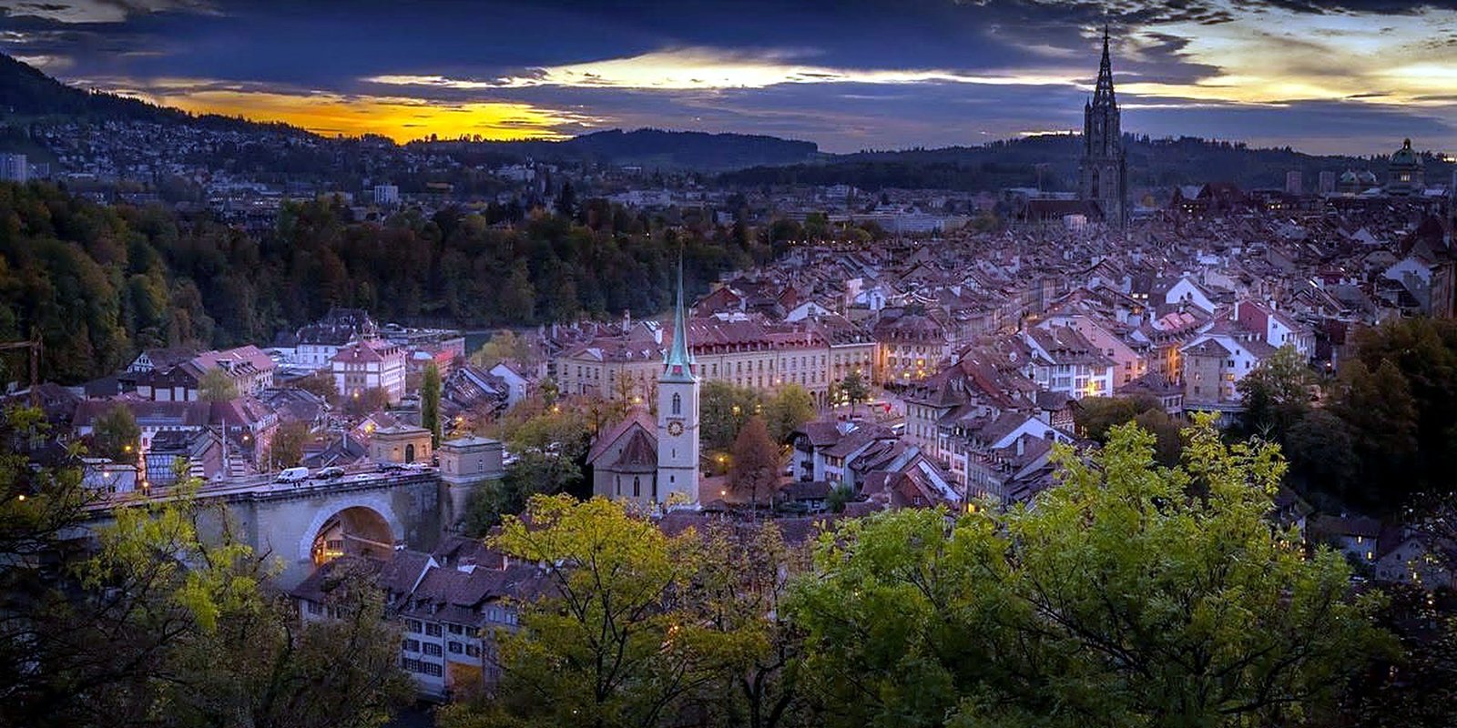 Vista panorâmica de Berna, na Suíça, ao entardecer, com a Igreja de Nydegg, a ponte sobre o rio Aare e a torre da Catedral