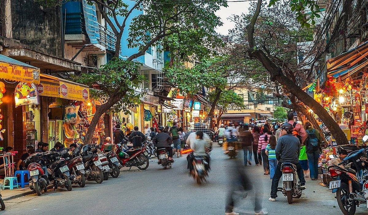 Rua do Bairro Antigo de Han&oacute;i com motos estacionadas, lojas e pedestres ao entardecer
