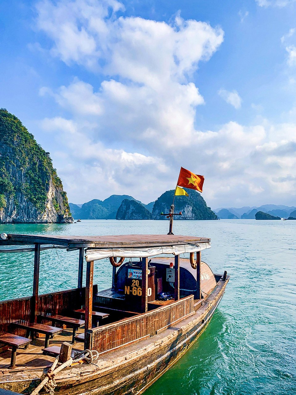 Barco de madeira com a bandeira do Vietn&atilde; na Ba&iacute;a de Ha Long, com ilhas ao fundo